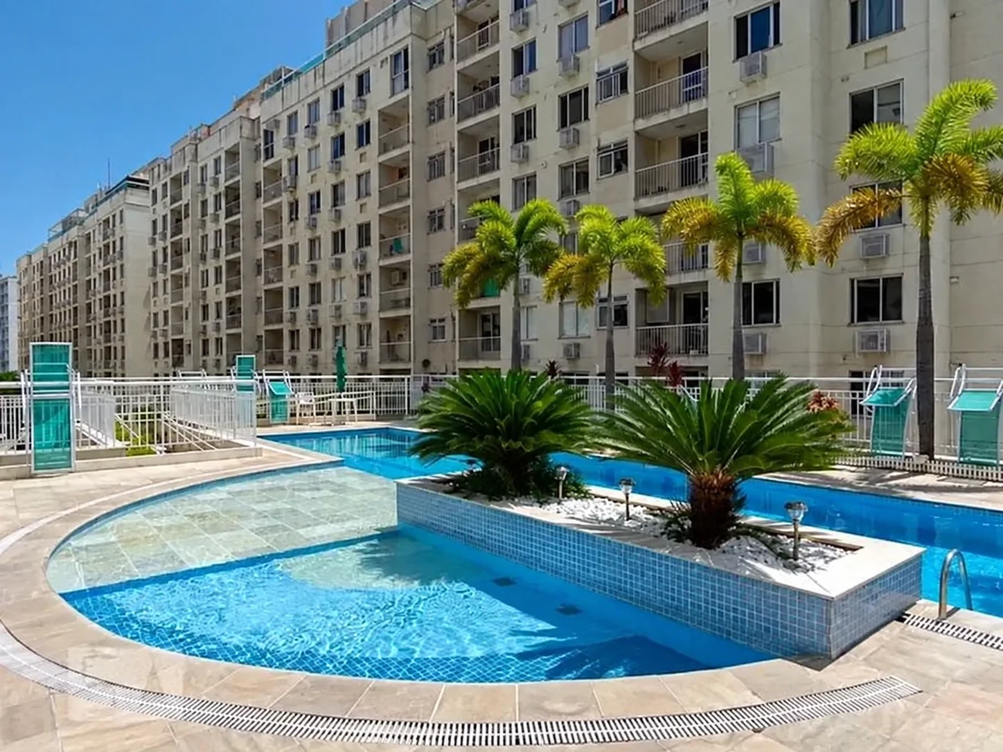 Piscina do Condomínio Ventura, com palmeiras e edifícios ao fundo